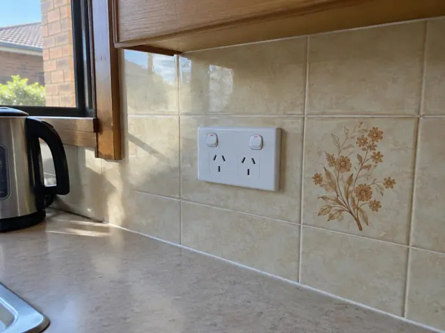 Double power point on beige tiled kitchen wall above a benchtop, with window and timber cabinetry in San Remo